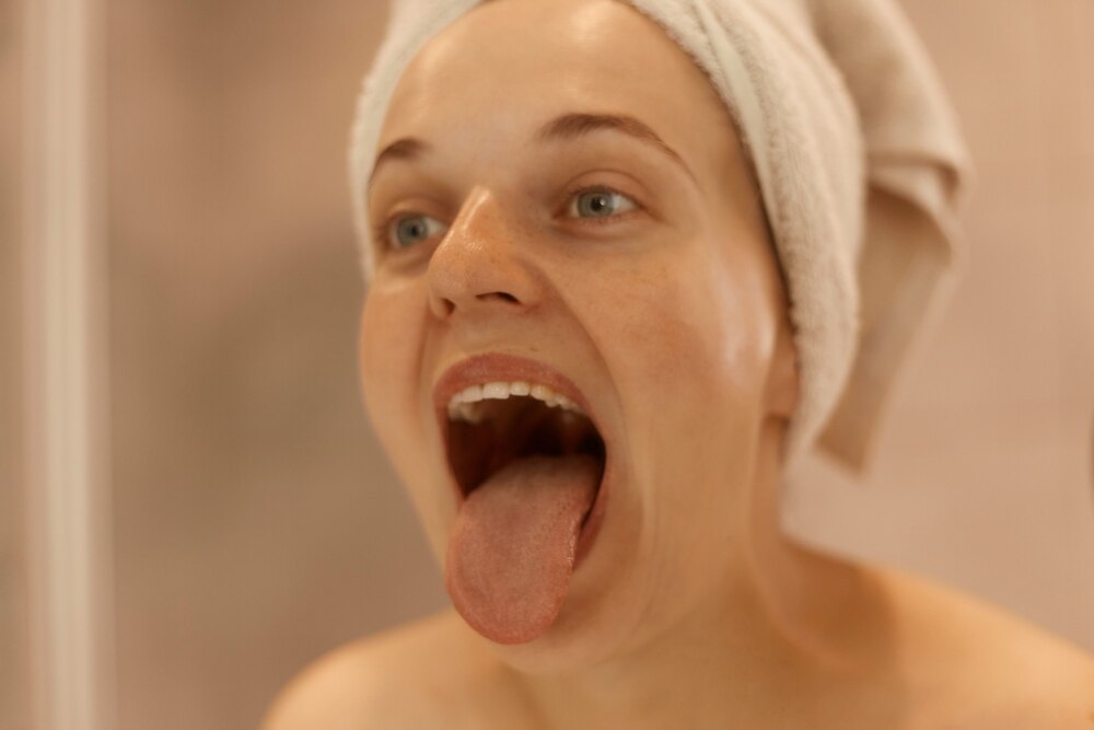 Close up portrait of young adult beautiful woman posing in bathroom, showing her tongue, being wrapped in white towel, doing hygienic procedures at home in morning.