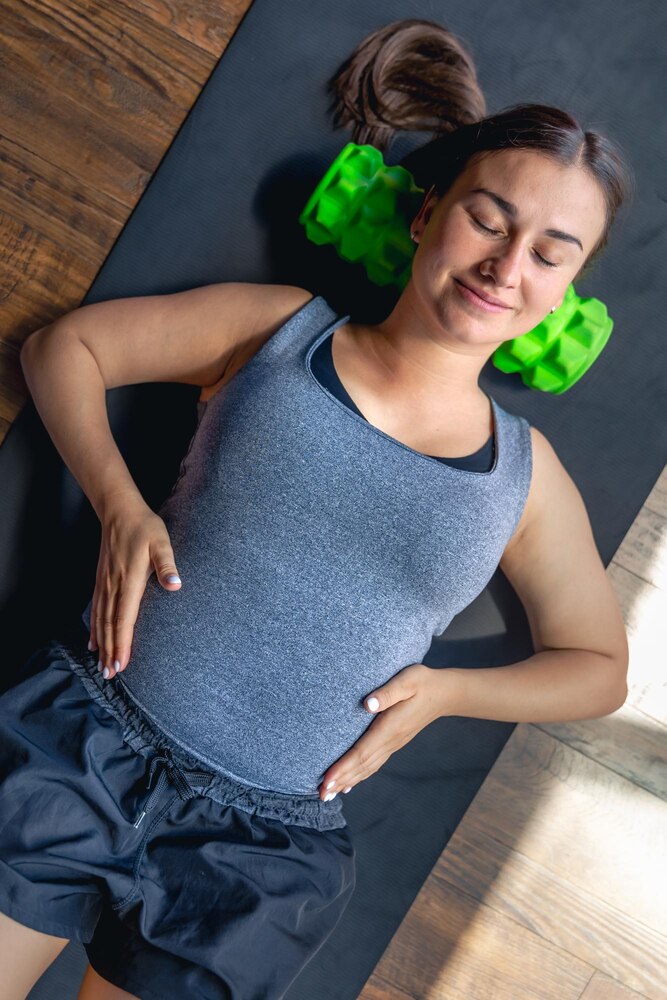 Pregnant woman in the gym on a mat with a massage roller